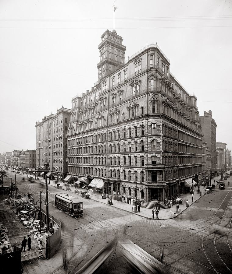 Black and white photograph of a tall ornate 19th-century office building on a busy street corner